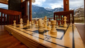 A chessboard with pieces set up on a wooden table inside a building with large windows overlooking mountains. - La kailasha Regency (Manali)