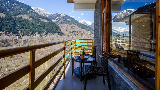 A balcony with a table and chairs, overlooking a mountainous landscape. - La kailasha Regency (Manali)