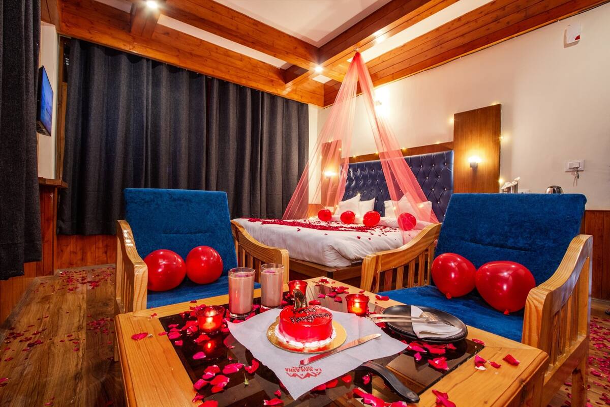 A room with a bed, two blue sofas, a wooden coffee table with a cake, candles, and red balloons.