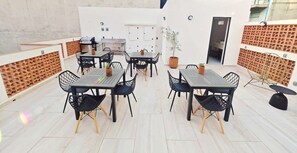 An outdoor patio area with multiple tables and chairs, a grill, and a potted plant.
