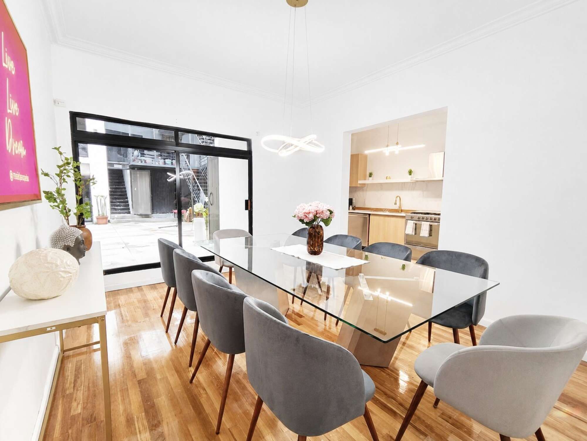 A modern dining area with a glass table, grey upholstered chairs, and a vase with flowers.