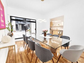 Uma sala de jantar moderna com mesa de vidro, cadeiras estofadas cinzas e um vaso com flores.