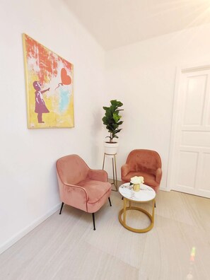 Quarto com duas poltronas cor-de-rosa, uma mesinha branca com base dourada e um vaso de planta.