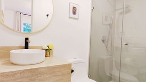 Un baño moderno con un lavamanos blanco, un inodoro y una ducha con cerramiento de vidrio.