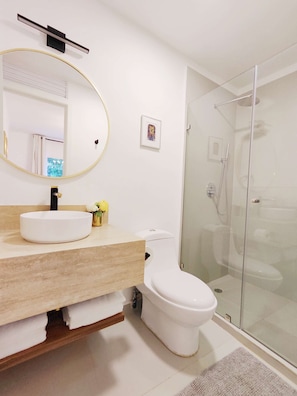 A modern bathroom with a white sink, a toilet, and a glass-enclosed shower.