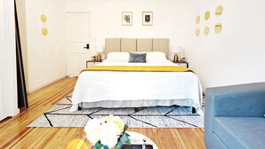 Una habitación de hotel con cama, mesitas de noche, una araña y un sillón azul.