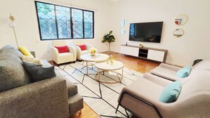 Un salon moderne avec un canapé, des fauteuils, une table basse, un téléviseur et une grande fenêtre.