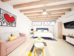 A modern bedroom with a bed, a sofa, a TV, and a ceiling fan.
