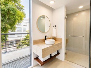 A modern bathroom with a glass shower, a round mirror, and a sink with a beige countertop.