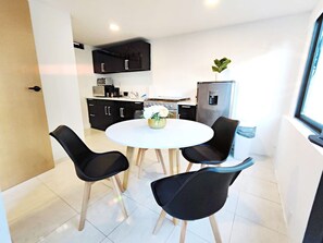 Une cuisine moderne avec des meubles de rangement noirs, une table à manger blanche et quatre chaises noires.