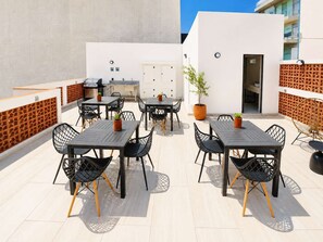 An outdoor patio area with multiple tables and chairs, a grill, and potted plants.