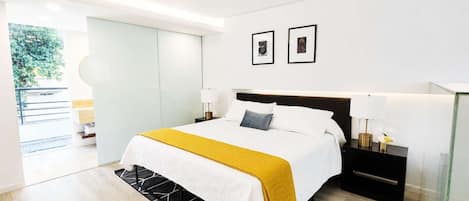 A modern bedroom with a bed, bedside tables, and a view of the outdoors.