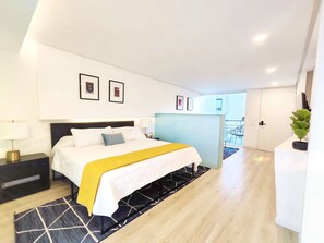 Une chambre d’hôtel moderne, équipée d’un lit, d’une table de chevet, d’une lampe et d’une œuvre d’art au mur.