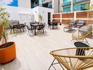 Un patio al aire libre con mesas y sillas, plantas en macetas y un cerco decorativo.