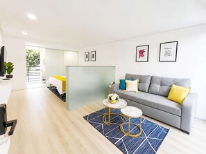 Una sala moderna con un sofá gris, una mesa de centro y una alfombra azul. Hay cuadros enmarcados en la pared y una planta en la esquina.
