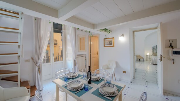 Un coin repas avec une table dressée pour quatre personnes, des chaises, une bouteille de vin et un tableau encadré accroché au mur.