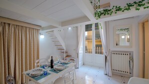 Un coin repas avec une table dressée pour deux personnes, des chaises blanches et un escalier menant à l’étage supérieur.