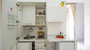 Une cuisine de taille réduite, avec des meubles blancs, un évier, une cuisinière et un petit réfrigérateur.