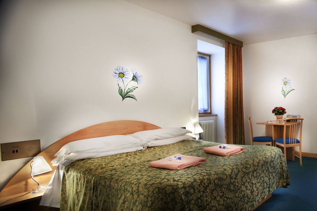 A hotel room with a bed, a desk, a chair, a lamp, and a window with curtains.