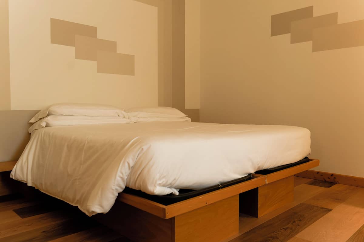 A single bed with a wooden frame and a mattress, positioned against a wall with a geometric design.