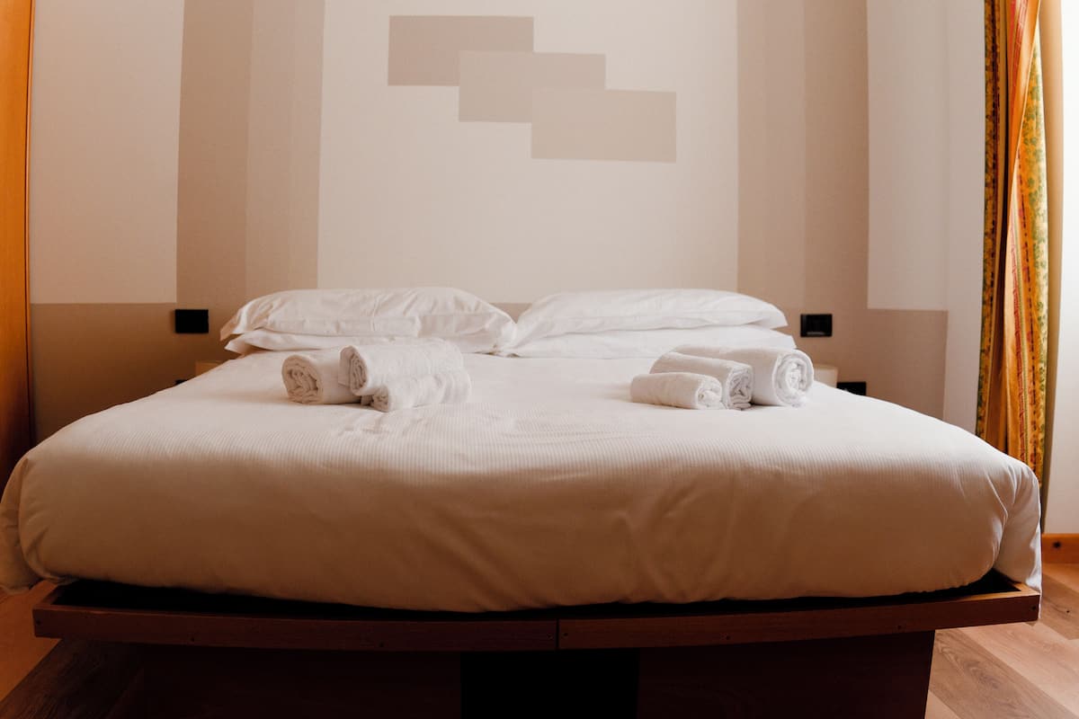 A neatly made bed with white linens and towels, a wooden headboard, and a wall with geometric patterns.