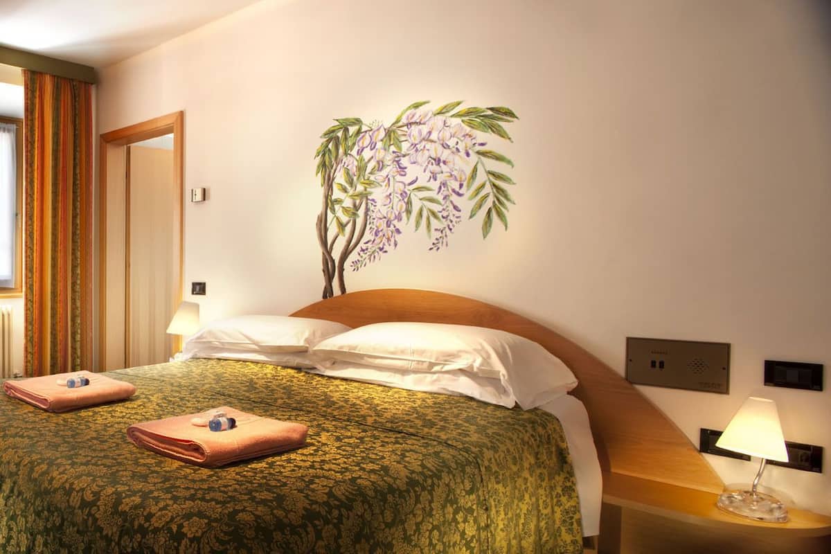 A hotel room with a bed, a desk, a chair, a wardrobe, and a wall-mounted plant.