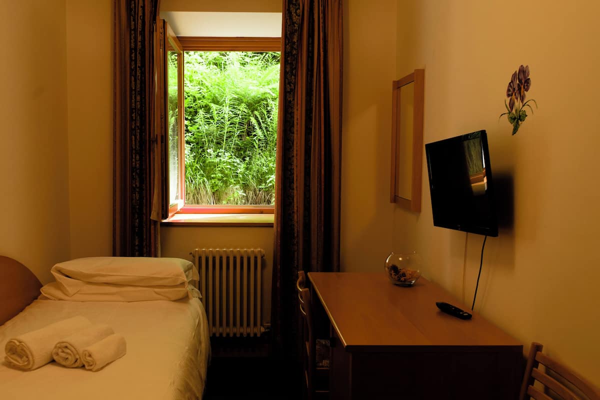 A hotel room with a bed, a desk, a radiator, a TV, and a window with curtains.