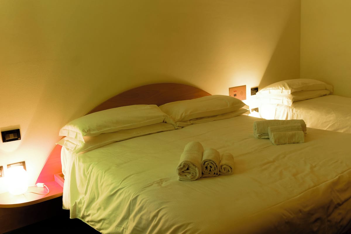 A hotel room with two beds, each with white linens and pillows, and two rolled towels on the beds.