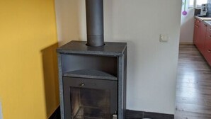 Moderni puukamiina, jossa on savupiippu, on sijoitettu kellertävän seinän viereen huoneeseen, jossa on laattalattia ja lähellä valkoinen ämpäri.