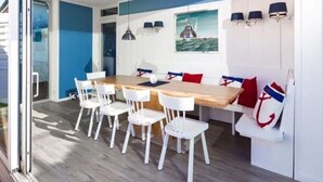 A dining area with a wooden table and white chairs, a painting of a sailboat, and a blue and white color scheme. - Frisian House Norderney (Norderney)