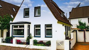 A white house with a steeply pitched roof, multiple windows, and a small balcony with red flowers. - Frisian House Norderney (Norderney)