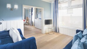 A modern living room with a blue sofa set, a TV on a glass stand, and a wooden floor. - Frisian House Norderney (Norderney)