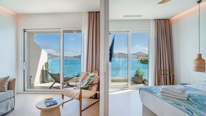 Een moderne hotelkamer met een grote schuifglazen deur naar een balkon met uitzicht op zee en bergen.