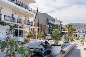 A coastal street with buildings, a parked scooter, and potted plants. - Ocean Rythm Elounda Apartment (Elounda)