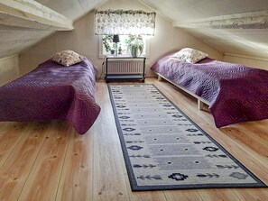 A room with two beds, a window with floral curtains, a radiator, and a patterned rug.