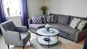 A living room with a grey sofa, a grey armchair, and a round coffee table with a vase of flowers. - 4 Star Holiday Home in Lysekil (Lysekil)