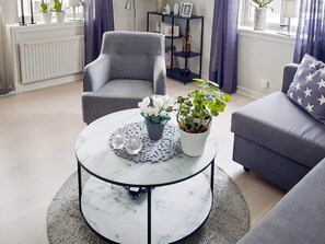 A living room with a round marble coffee table, grey armchairs, a grey sofa, and a potted plant.