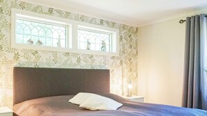 A bedroom with a bed, a nightstand, a window with decorative glass panes, and a curtain. - 4 Star Holiday Home in Lysekil (Lysekil)