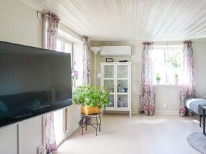 Ein Wohnzimmer mit einem Flachbildfernseher, einer Vitrine, einer Pflanze auf einem kleinen Tisch und einem Sofa.