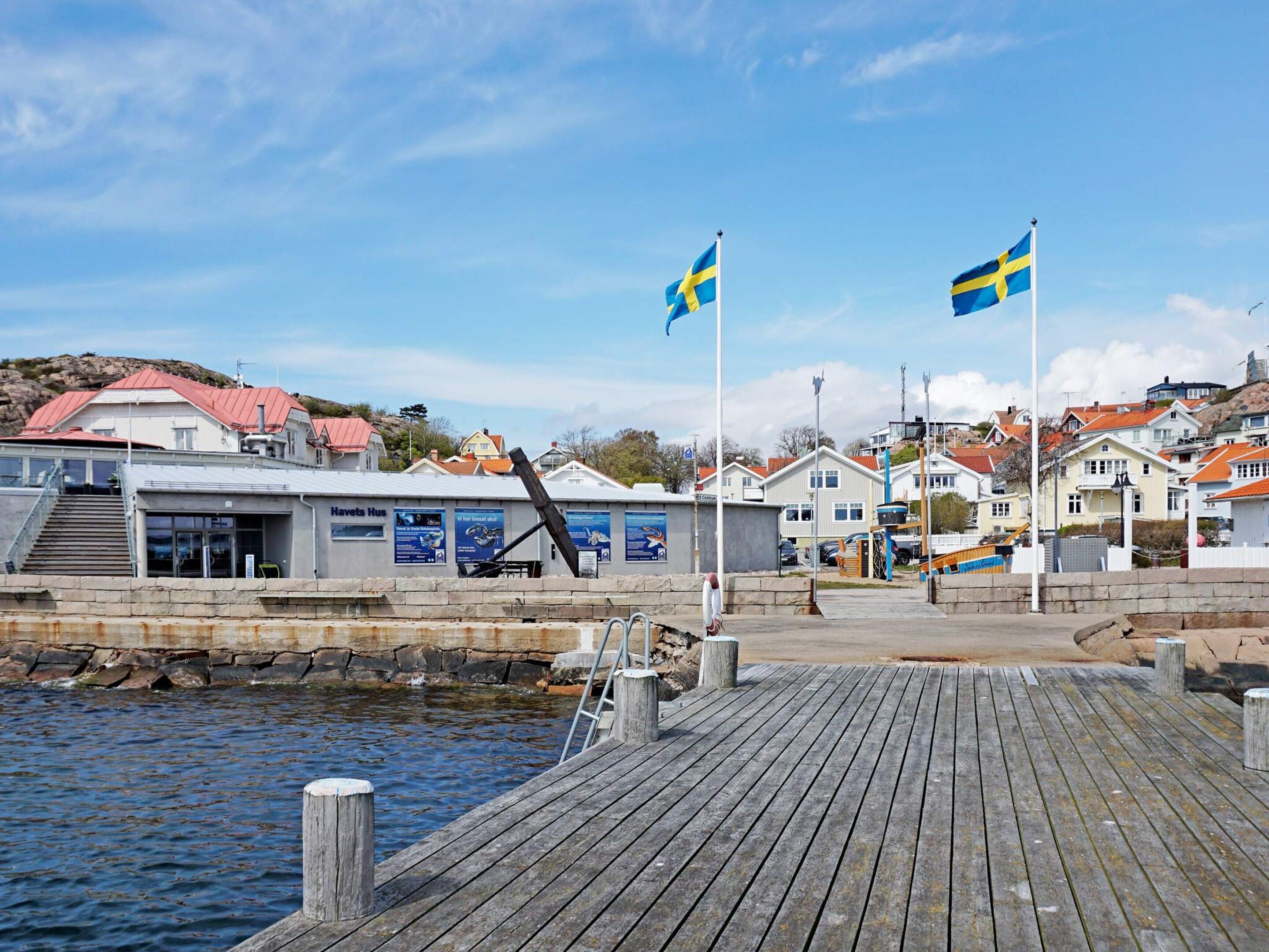 A wooden pier leading to a building with a red roof, a sign reading 'Havets Hus,' and two Swedish flags.