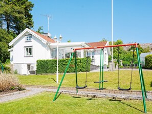 A residential area with a white house, a swing set, and a well-maintained lawn. - 4 Star Holiday Home in Lysekil (Lysekil)