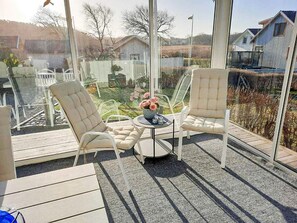 A sunlit outdoor seating area with two cushioned chairs and a small table, overlooking a garden and residential buildings. - 4 Star Holiday Home in Lysekil (Lysekil)