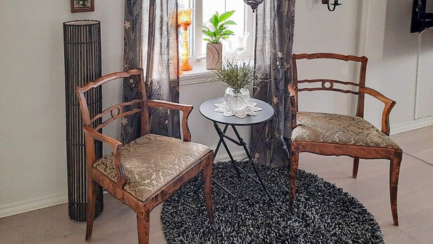 A room with two wooden chairs, a small round table, a potted plant, and a tall floor lamp. - 4 Star Holiday Home in Lysekil (Lysekil)
