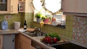 Eine Küche mit Spüle, Arbeitsplatte und Schränken. Auf der Fensterbank stehen Blumentöpfe und auf der Arbeitsfläche eine Weinflasche.