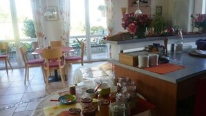 Eine Küche mit Essbereich, ausgestattet mit einem Tisch und Stühlen, einer Küchenarbeitsplatte mit Gläsern und Flaschen sowie einem Blick durch große Fenster.
