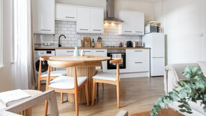 A modern kitchen with white cabinets, a round wooden table, and a built-in washing machine. - Centrally located Scandinavian high quality design. 2 min walk to station (London)