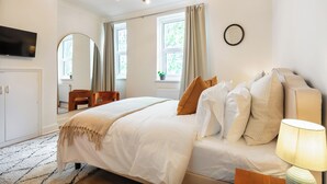A bedroom with a bed, a TV, a lamp, and a window with curtains. - Centrally located Scandinavian high quality design. 2 min walk to station (London)