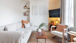 A modern living room with a sofa, a coffee table, a rocking chair, and a TV. There are shelves with decorative items and a plant on the wall. - Centrally located Scandinavian high quality design. 2 min walk to station (London)