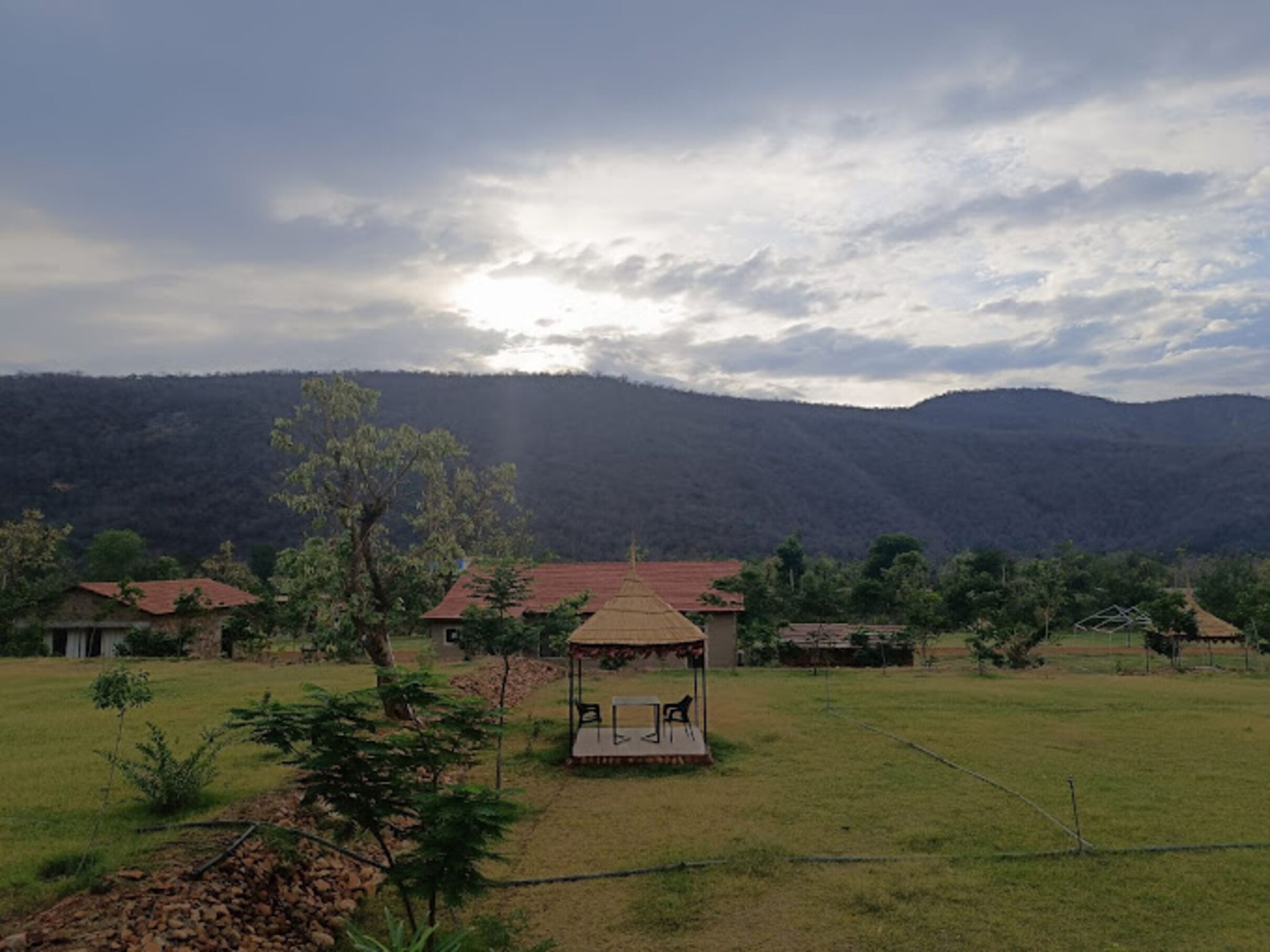 A rural landscape with a gazebo in the foreground, surrounded by open fields and a mountain range in the background.