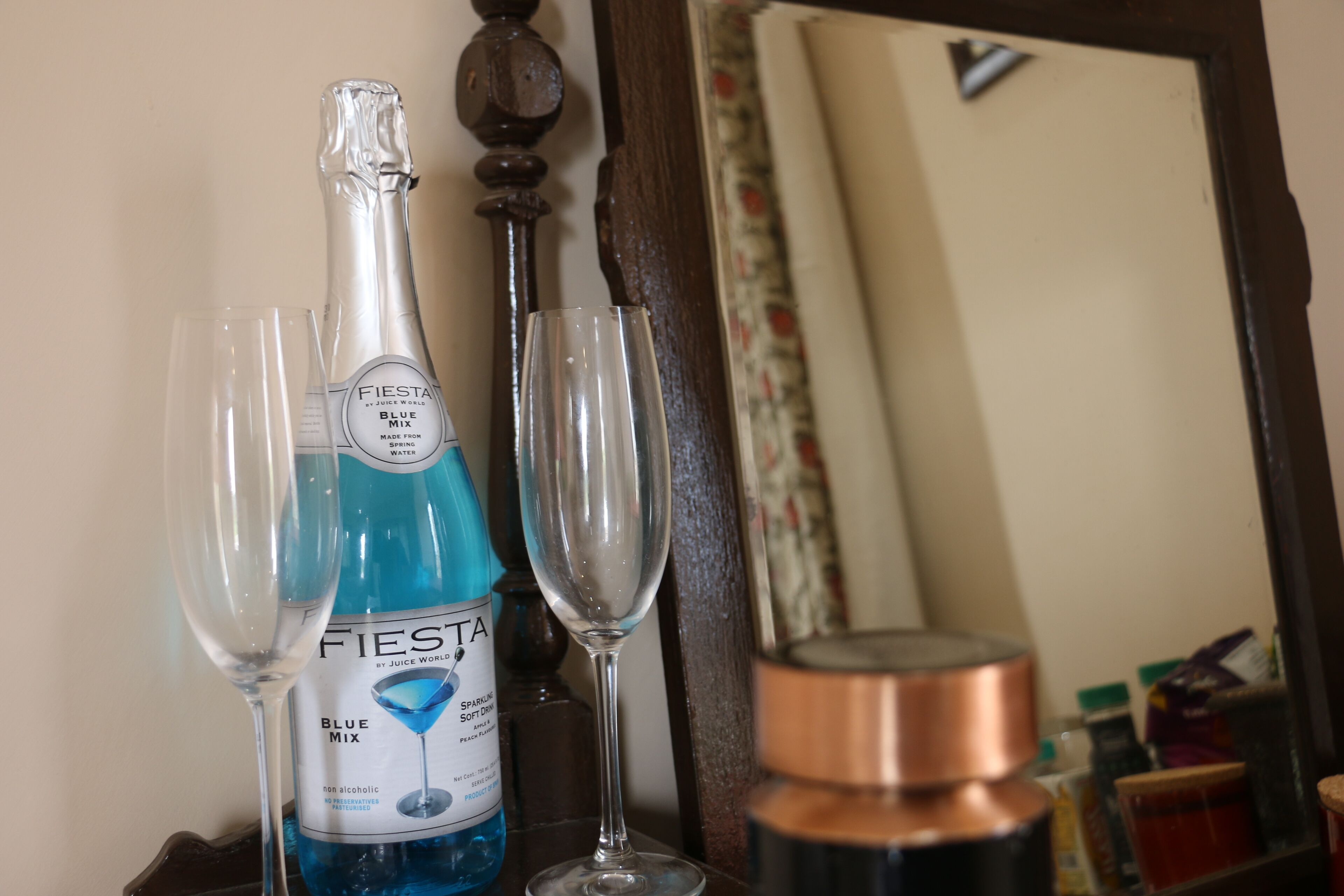 Una botella de champán Fiesta Blue Mix, dos copas y un recipiente de cobre sobre una superficie de madera.